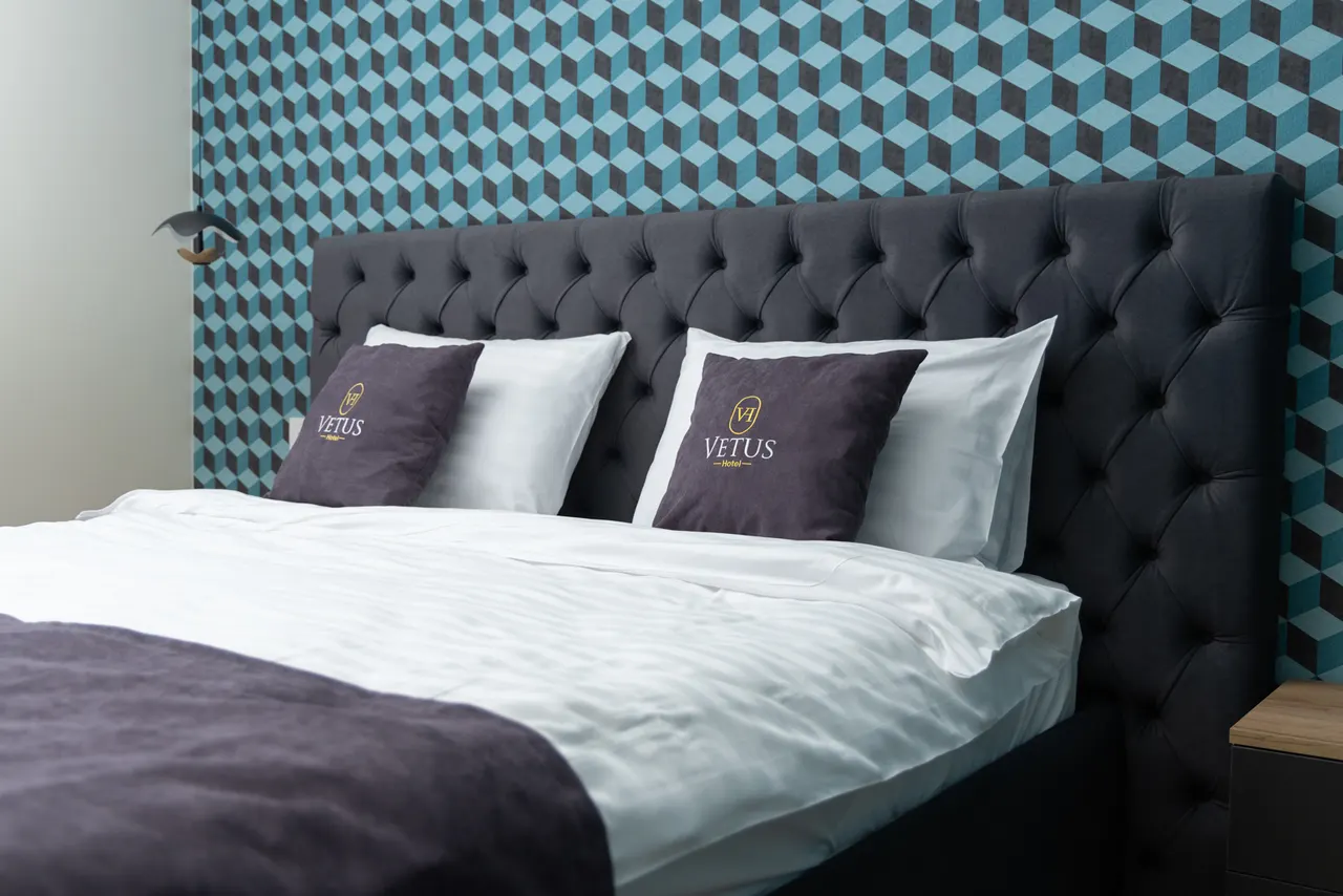 Suite bed with Vetus pillows against the teal geometric wall
